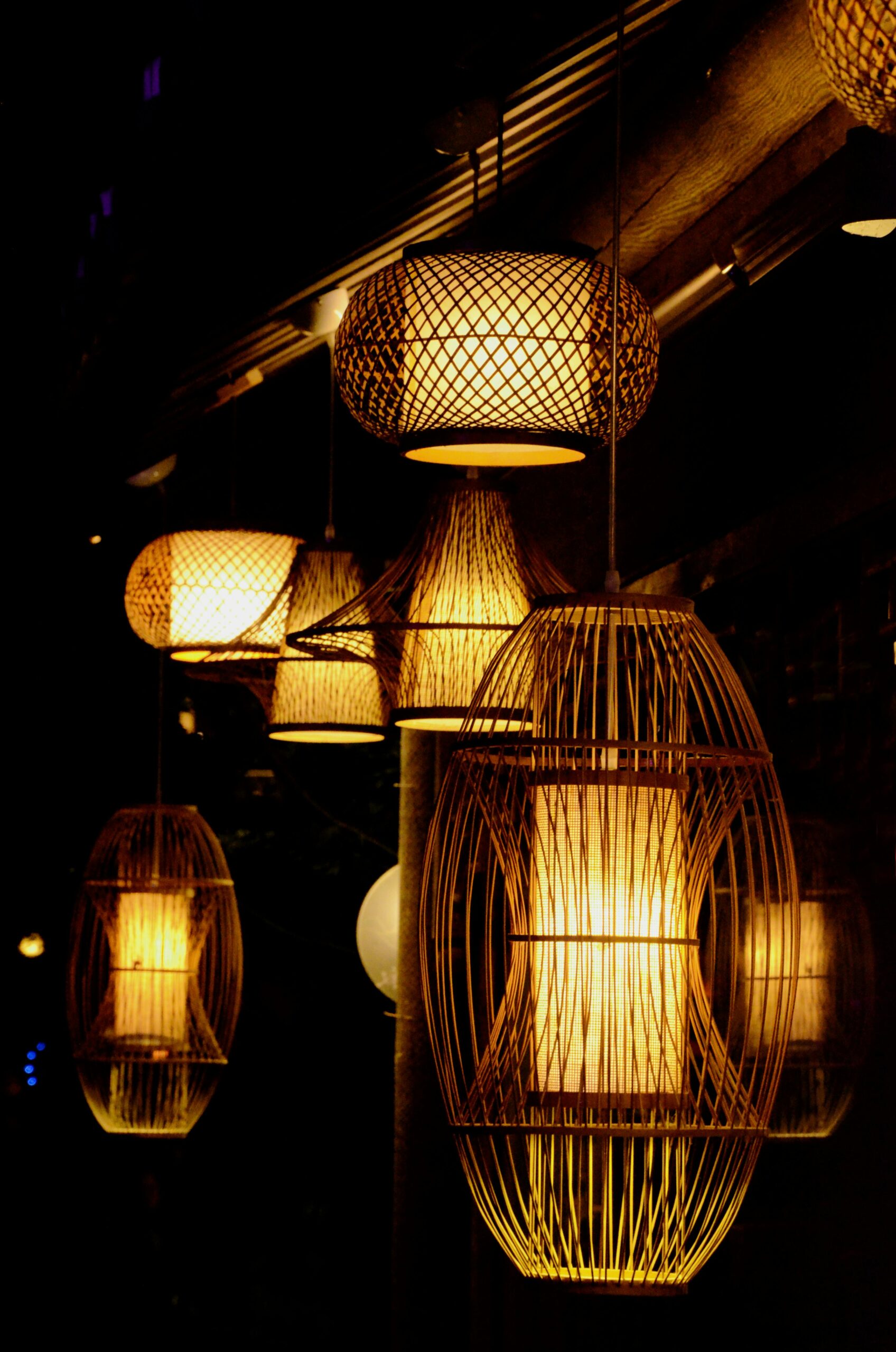 A series of bamboo lanterns providing warm illumination in a dark setting, showcasing intricate wicker designs.