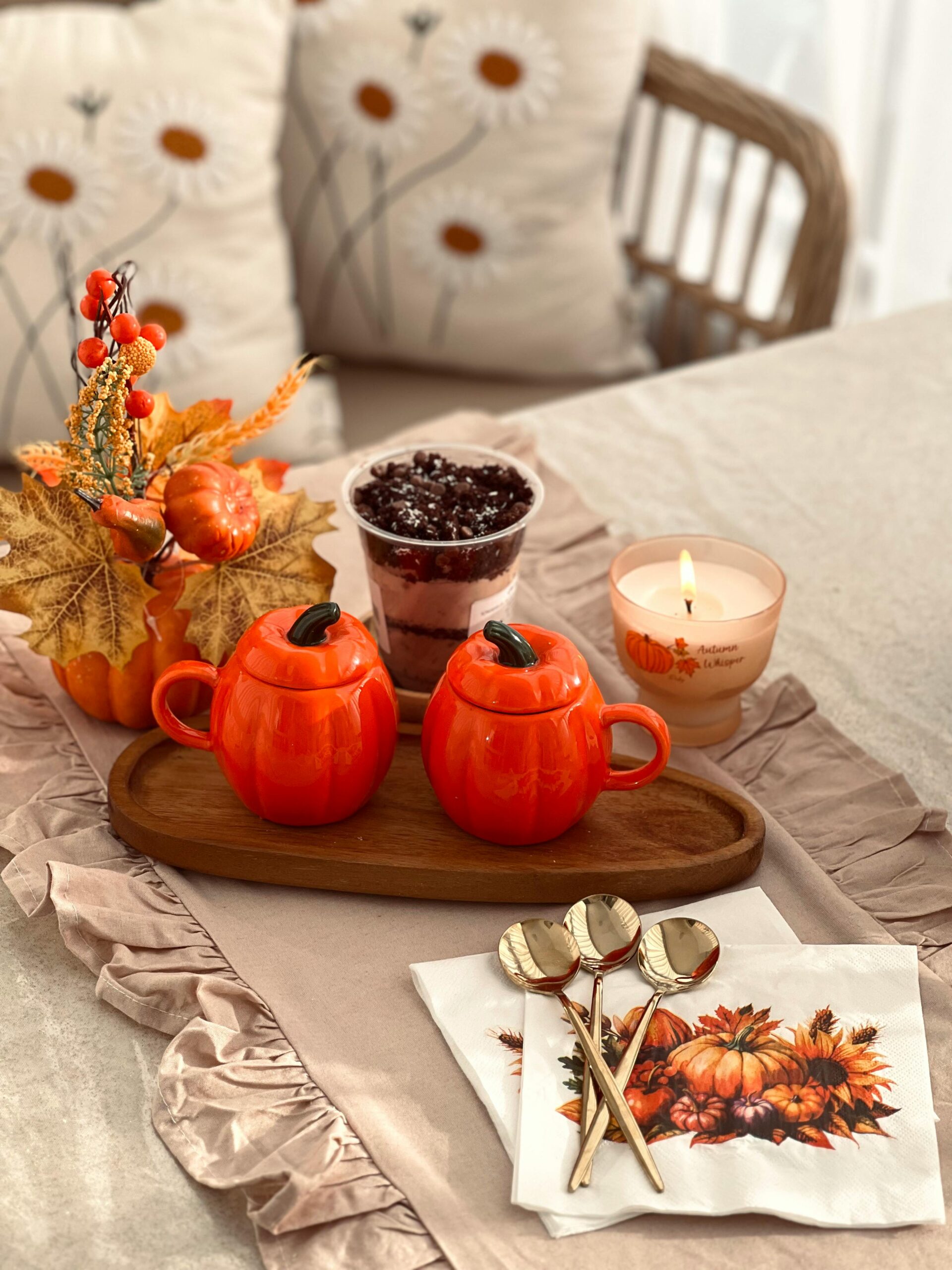 Warm autumn decor with pumpkin mugs, candles, and fall foliage on a table.
